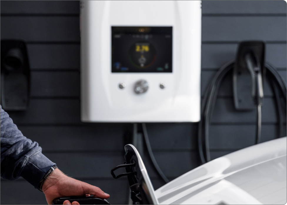 Person plugging an electric vehicle into a charging station mounted on a dark wall, showcasing the seamless work of an electrician in Vancouver, WA.